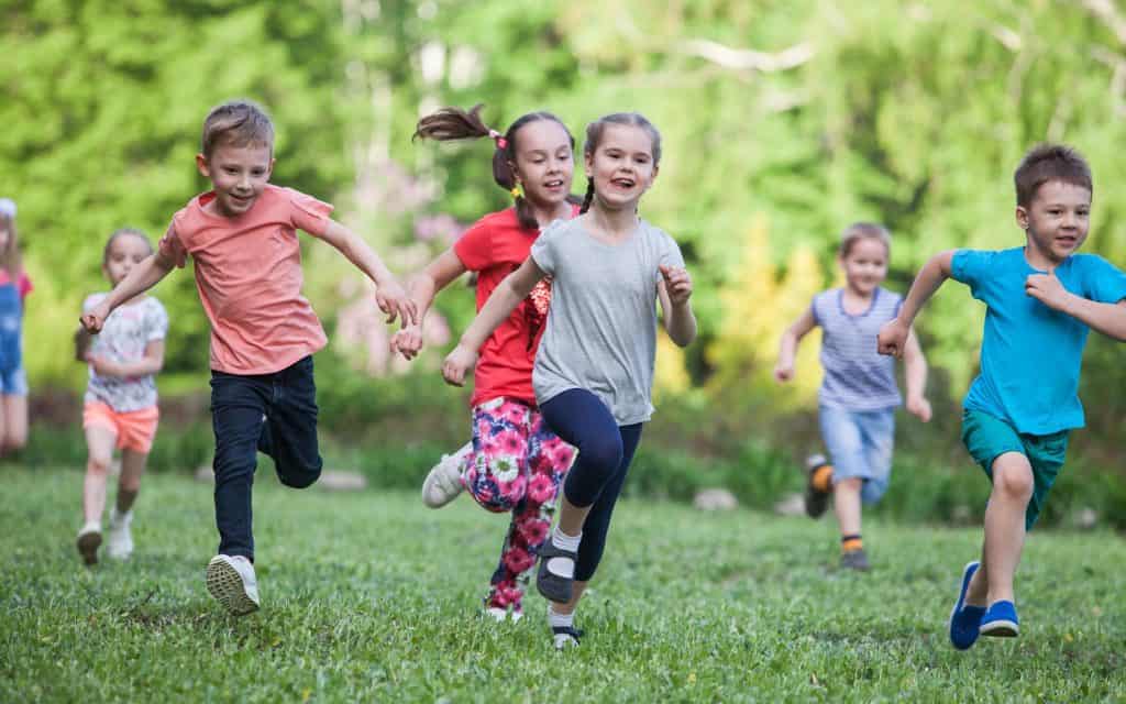 Various children running through grass field