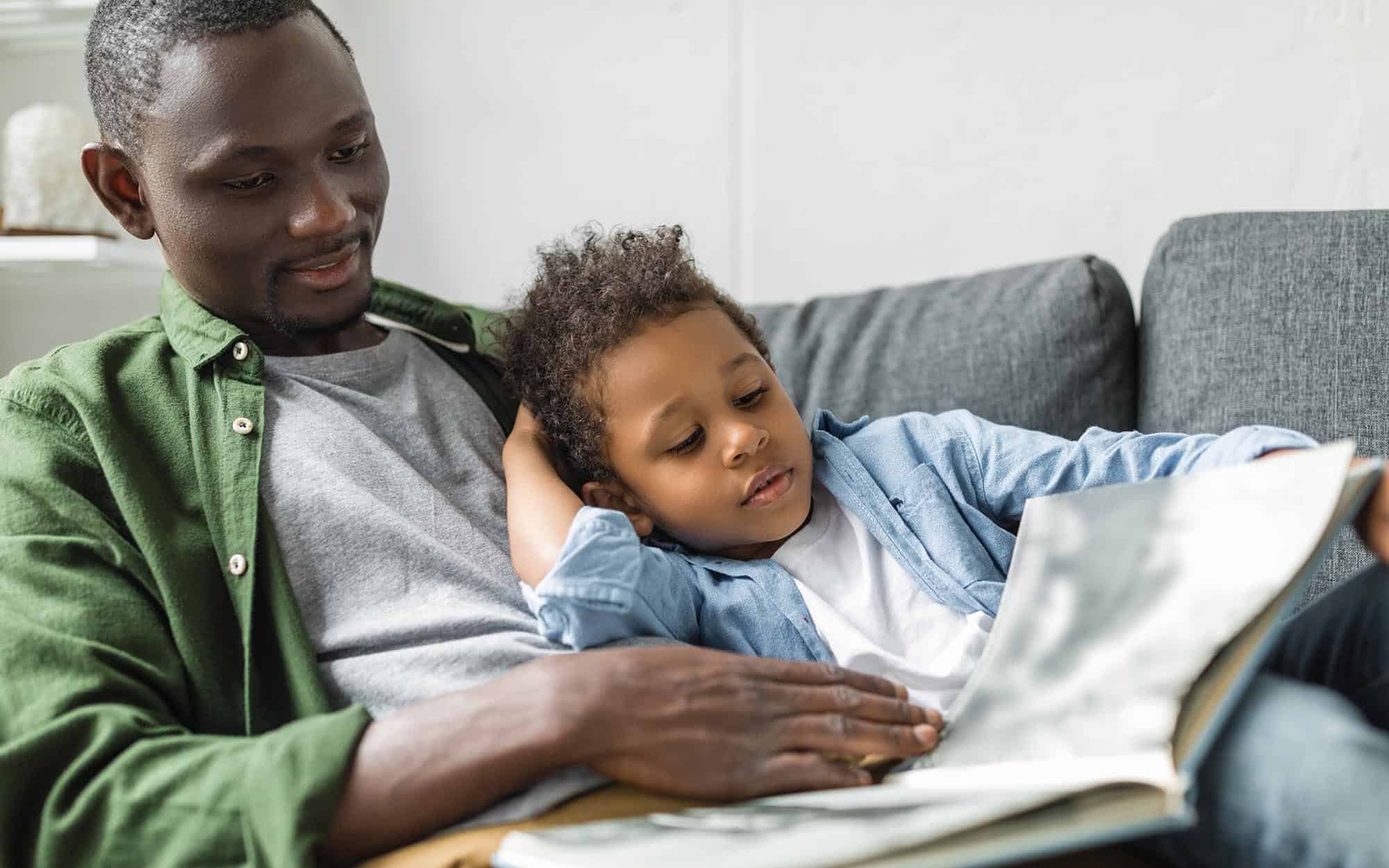 A parent and child on couch reading a book together