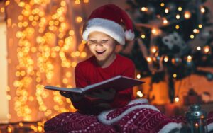 Front view of a child wearing a santa hat and reading a book