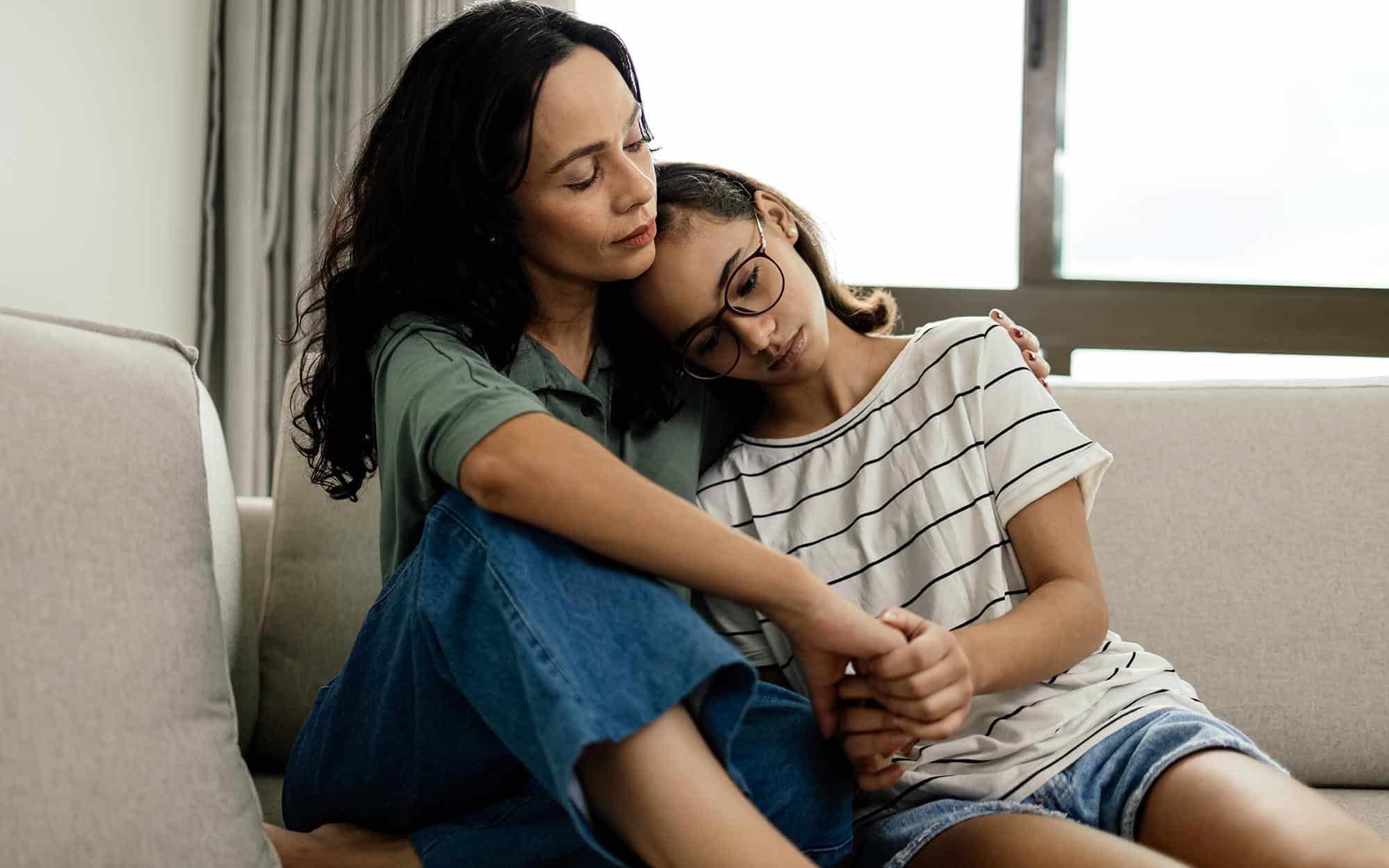 Front view of a mother hugging her daughter while sitting on the couch