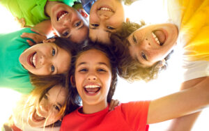 Group portrait of happy kids huddling, looking down at camera and smiling