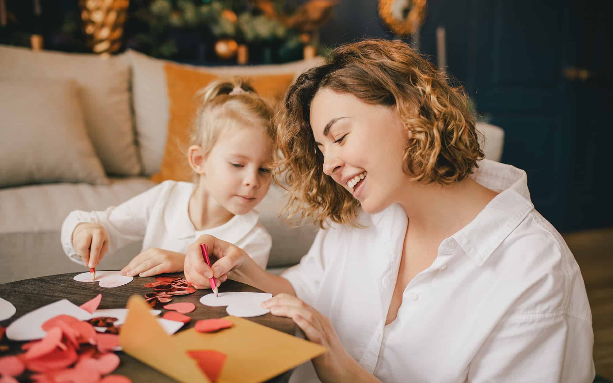 Side view of a woman and young girl cutting out paper hearts for Valentines Day