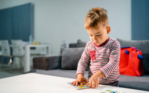 Small boy little playing at home alone by the table with puzzle developing mental skill