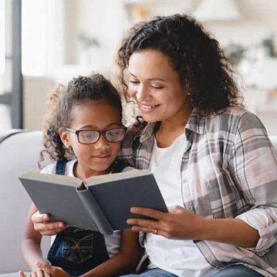 African-american mother mom reading fairy tales book novel with daughter girl, learning together, helping assisting with homework for school. Female tutor teaches schoolgirl at home. Homeschooling